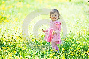 A little girl in a pink dress is laughing in a clearing with dandelions.