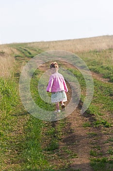 Little girl in a pink dress walking along a road