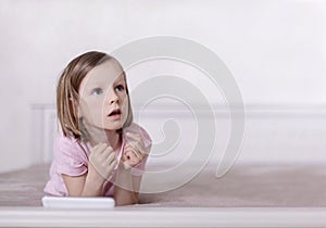 Little girl in pink pajamas on the bed is looking at a smartphone