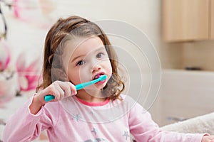 Little girl in pink pyjamas in bathroom brushing teeth