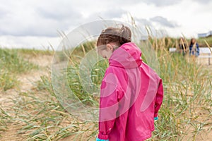 Little girl in a pink raincoat stands on the sand dunes
