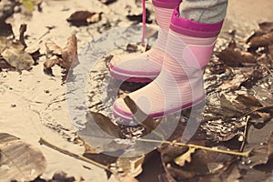 Little girl with pink rubber boots standing in puddle