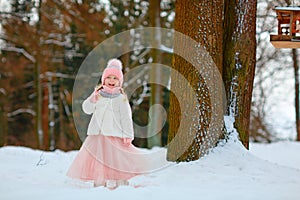 Little girl in a pink skirt in winter smiles in the park