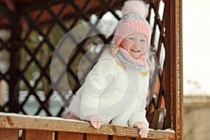 A little girl in a pink skirt in winter smiles in a park in a ga