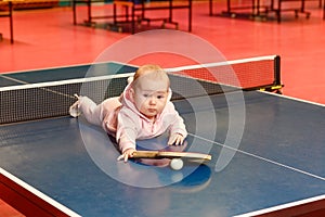 A little girl in a pink suit is lying on a tennis table