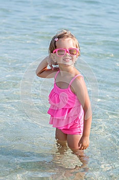 Little girl in pink swimsuit and sunglasses at the sea posing camera. Happy, smiling. Summer vacation.