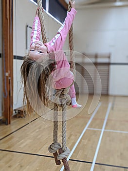 Little girl in pink swinging from ropes in the school gymnasium