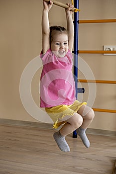 Little girl in a pink T-shirt Holds her hands on the crossbar. Playground