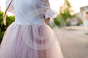 Little girl in pink tutu skirt standing outdoor from behind