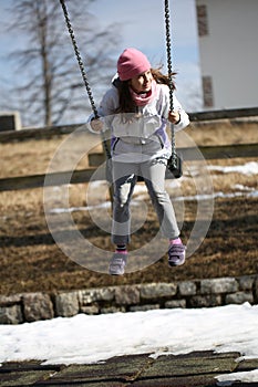 Little girl with pink wool cap has fun on the swing in the playg