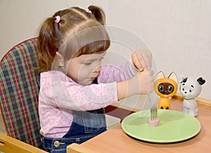 The little girl pins sausage on a fork