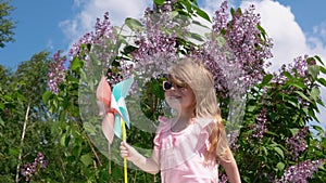 Little girl with a pinwheel in a park next to a blooming lilac in the spring.