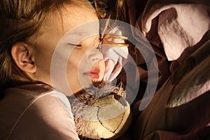 Little girl in pjamas with teddy bear lie down on bed while sun shine through the window