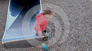 Little girl with plait in pink hoodie plays on slide in park