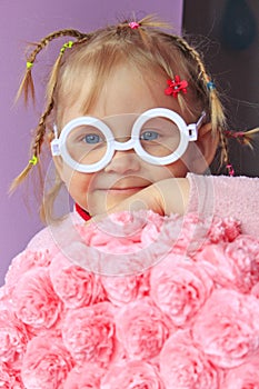 Little girl in plastic glasses smile near paper flowers made from papier-mache