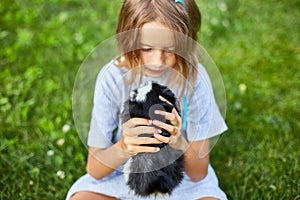 A little girl play with Black Guinea pig sitting outdoors in summer