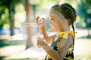 Little girl play in park blow soap bubbles profile close up