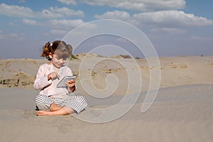 Little girl play with tablet pc in desert