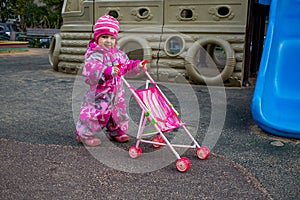 little girl play walking with toy stroller on children plyground in winter cold