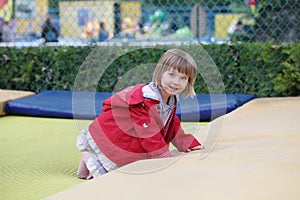 Little girl on playground in a park, jumping on trampoline. Little Girl seating on a Trampoline