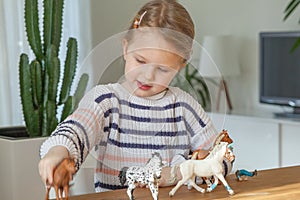 Little girl playing with animal toys on a wood table in living room