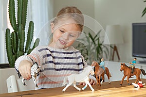 Little girl playing with animal toys on a wood table in living room