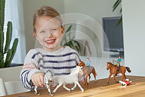 Little girl playing with animal toys on a wood table in living room