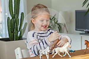 Little girl playing with animal toys on a wood table in living room