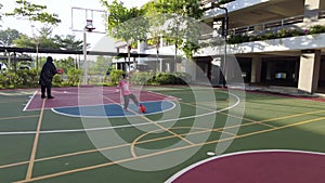 Little girl playing ball at the basketball court with mother
