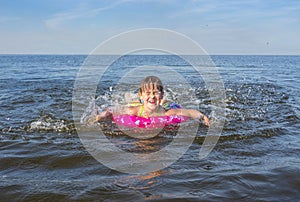 A little girl playing on the beach with splashing sea waves.  Summer holidays and healthy lifestyle concept