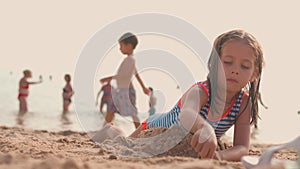 Little girl playing on beach on summer vacation with people on background