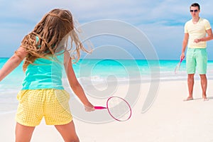 Little girl playing beach tennis on vacation with dad