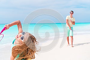 Little girl playing beach tennis on vacation with young father