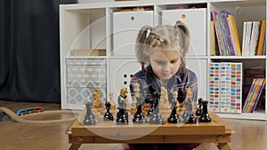A little girl playing chess. The child plays chess at home, The development of logical thinking in children.