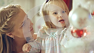 Little girl playing with Christmas toy near the Christmas tree with mother