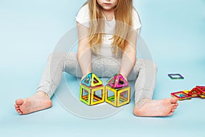 Little girl playing with colorful magnetic constructor toy on blue background. child built a house