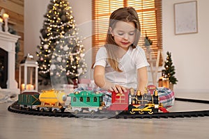 Little girl playing with colorful train toy in room decorated for Christmas
