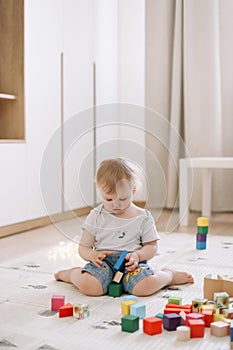 Little girl playing with colorful wooden brickes on the floor in the kids room