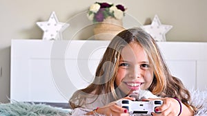 A little girl is playing a computer console on a sofa in a bright room. Concurrent games for children. Joystick for