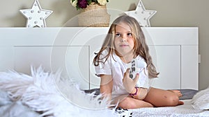 A little girl is playing a computer console on a sofa in a bright room. Concurrent games for children. Joystick for