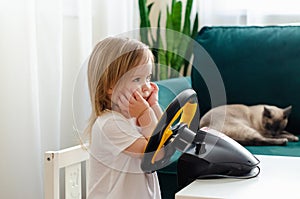 Little girl playing with a computer steering wheel. Little girl playing video game - car racing. Future driver. Getting