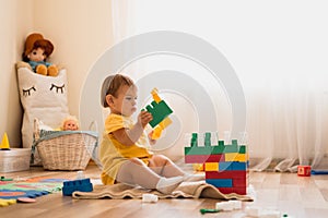 Little girl playing with construction toy blocks building a tower in a sunny kindergarten room