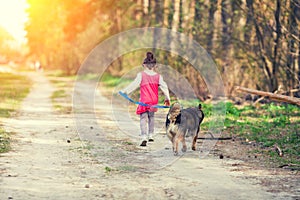 Little girl playing with a dog running on dirt road along forest