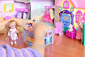Little girl playing with dolls. Girl lays a doll down to sleep on a bed. Colorful toy set on a table
