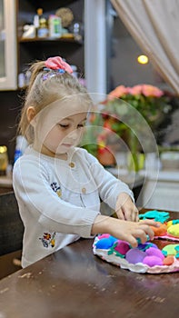 A little girl playing with Easter eggs from play dough decoration with beads. Cute children& x27;s crafts for Easter