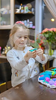 A little girl playing with Easter eggs from play dough decoration with beads. Cute children& x27;s crafts for Easter