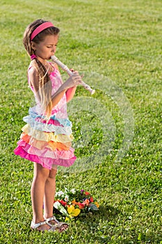 Little girl playing a fife on the green grass with