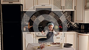 A little girl is playing with flour and dough in the kitchen,she claps her hands