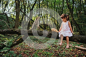 Little girl playing with her bear in the woods. girl sitting on