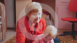 Little girl playing with her grandmother on the floor, grandma hugging and kissing granddaughter